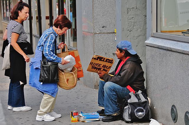 A photo of people donating money to a homeless man.